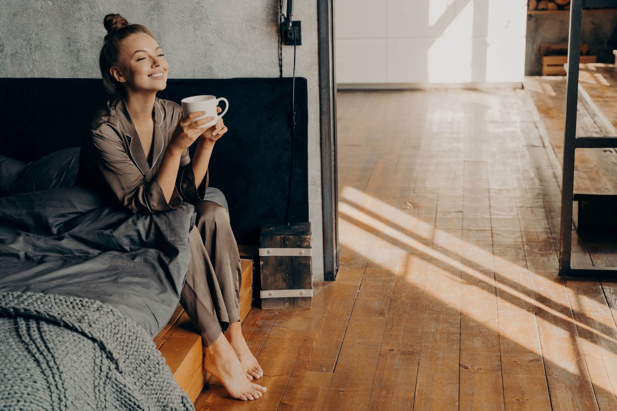 woman holding a cup of coffee while sitting on the bed