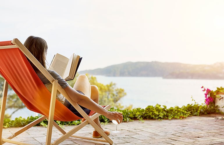 woman sitting on a chair reading a book in front of a lake