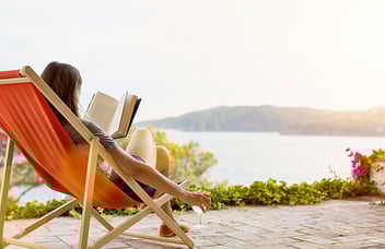 woman sitting on a chair reading a book in front of a lake