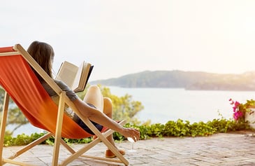 woman sitting on a chair reading a book in front of a lake