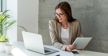 woman looking at her laptop and holding an ipad